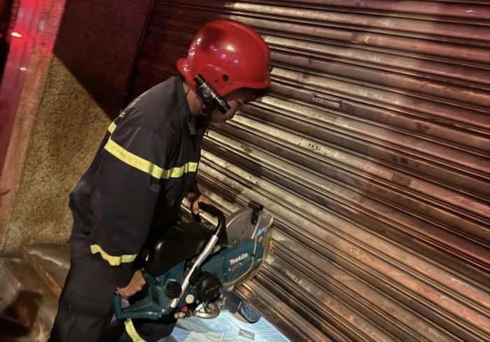 Cảnh sát chữa cháy đang tích cực sử dụng máy cắt để phá cửa cuốn.